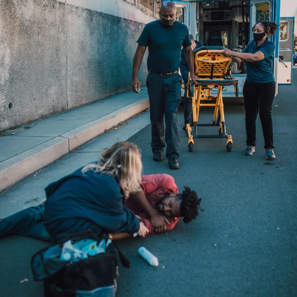 Paramedics assist an injured person on a roadside, showcasing emergency healthcare in action.